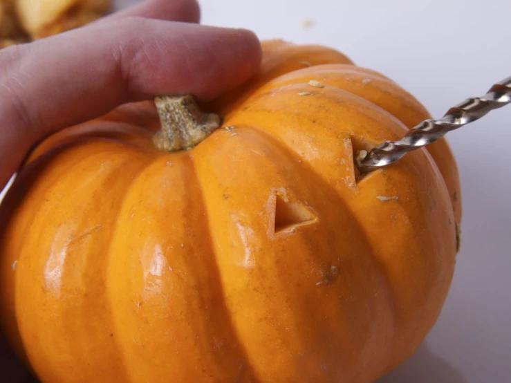 a small pumpkin being cut by a person with two tongs