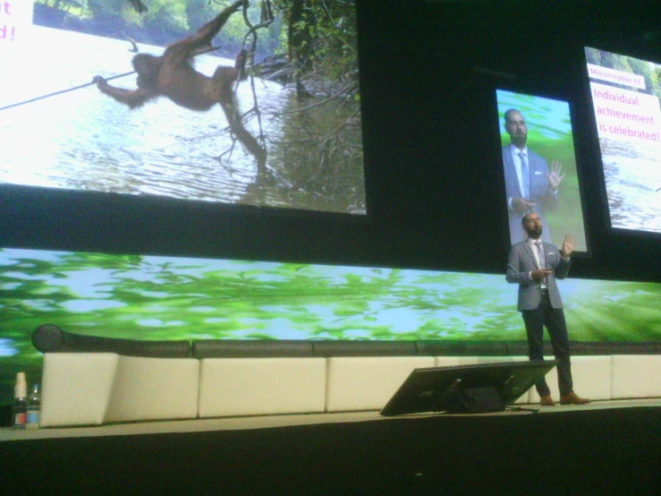 a man stands on stage, looking at a projection