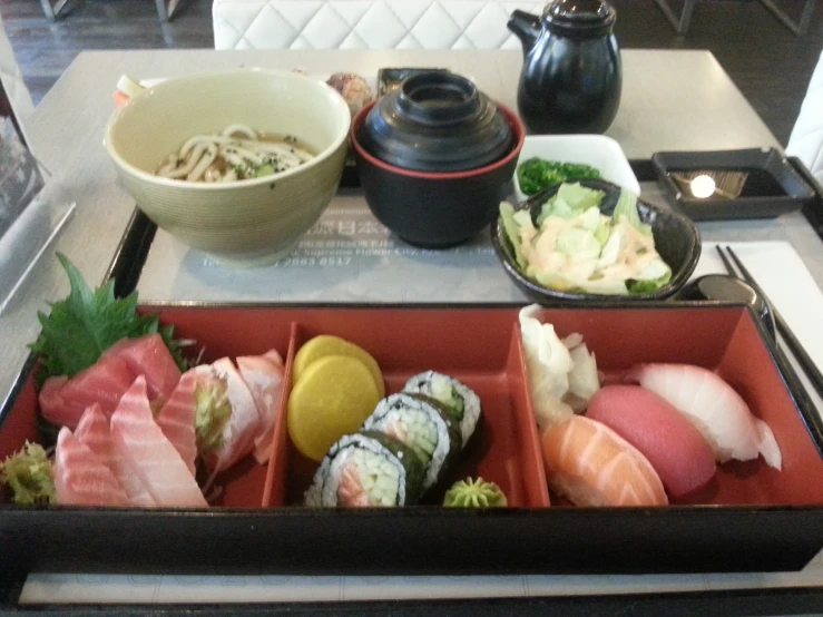 a red tray filled with sushi, noodles and vegetables