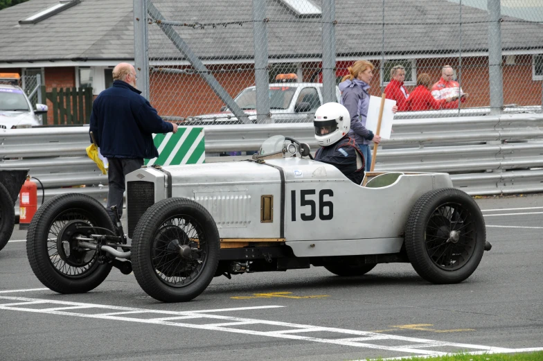 an older style race car with a helmet parked next to some people