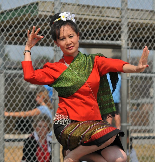a woman wearing a red shirt and colorful skirt dances in front of people