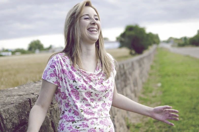 a woman poses by the side of a stone wall