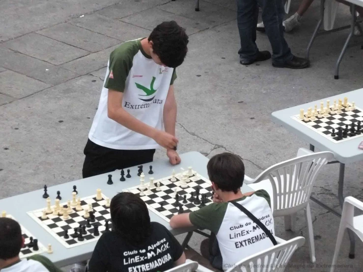 two children and a person are playing chess on the pavement