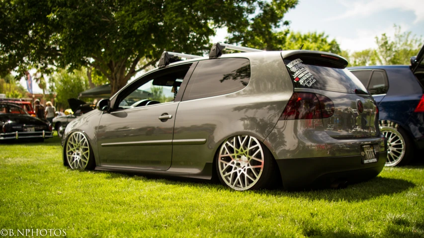 a hatchback sits on the grass next to other cars