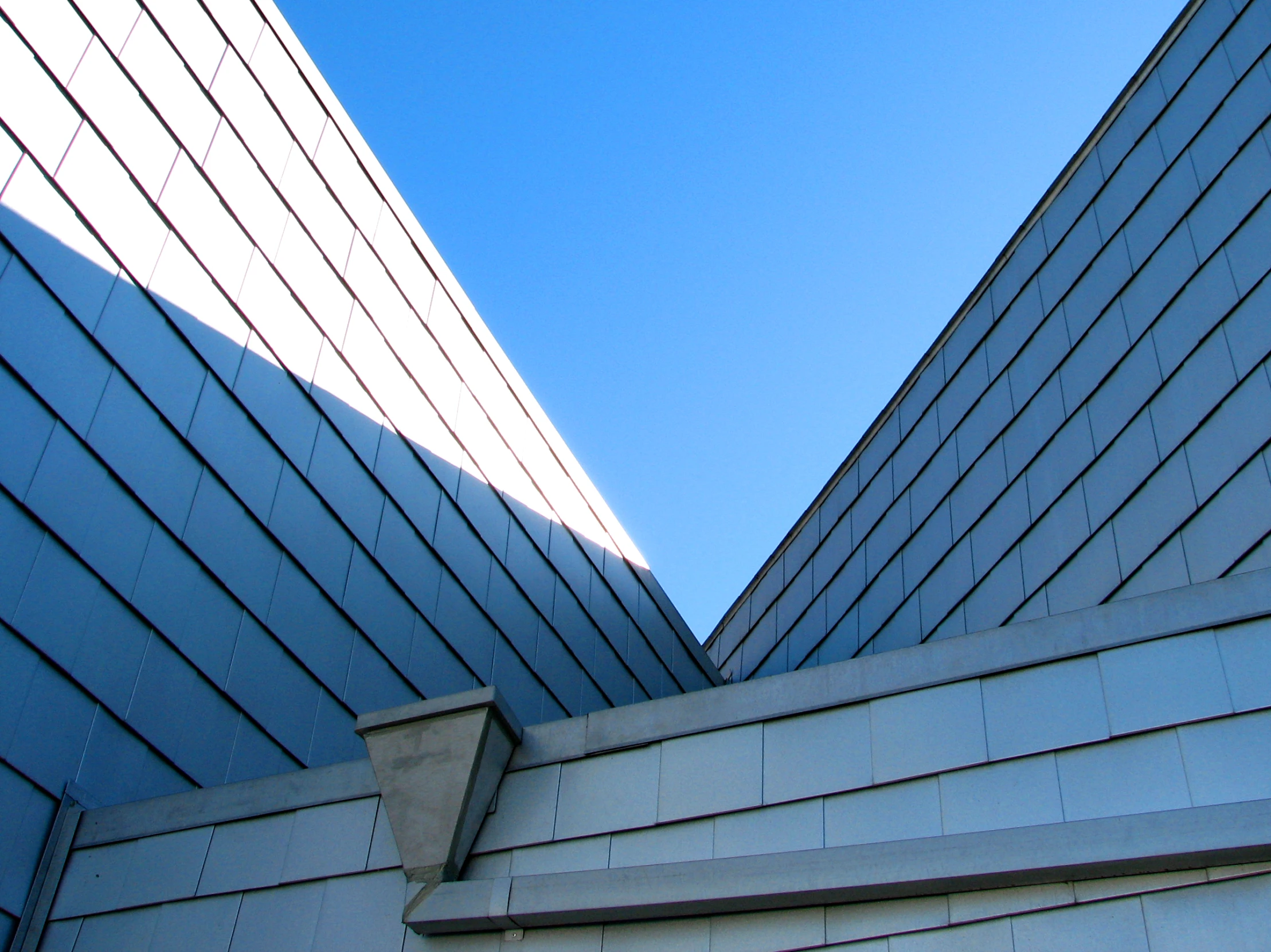 upward view of a wall and a blue building with slanted glass windows