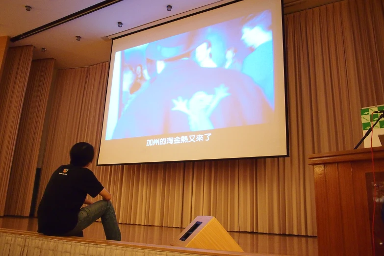 a person is sitting on the bench watching a projected po