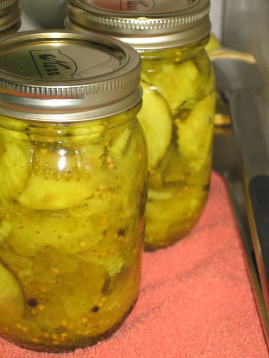 three jars full of pickles sit on a  board