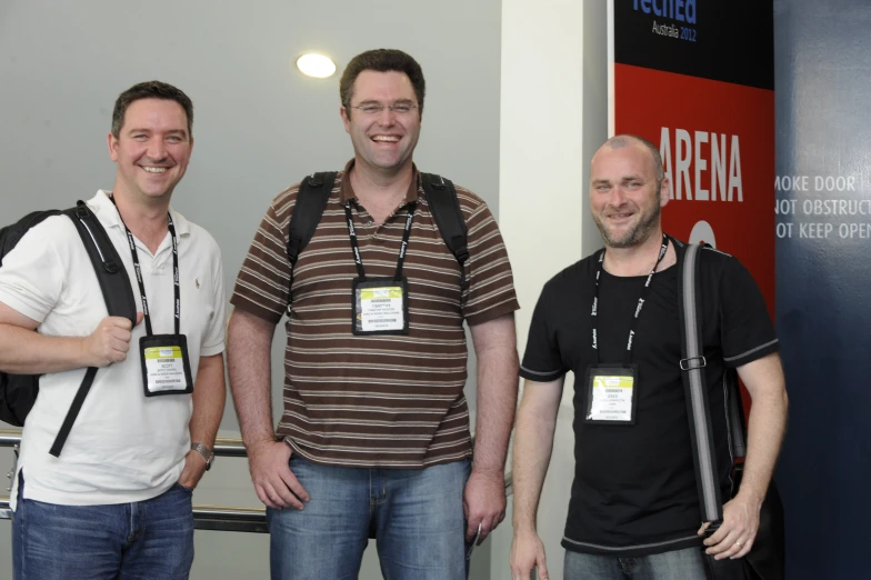 three men smiling with a camera around their neck