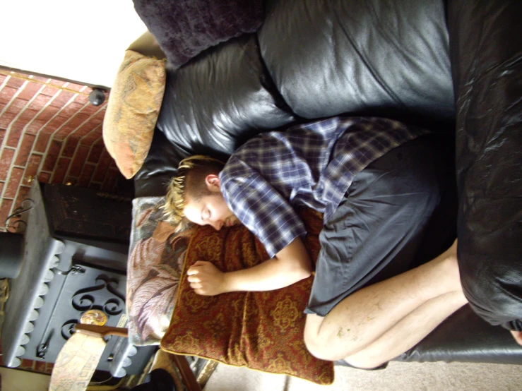 a man in plaid shirt sleeping on couch next to fire place