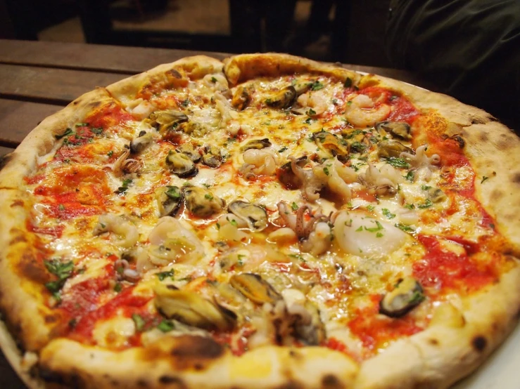 a pizza with cheese and shells on it sitting on a wooden table