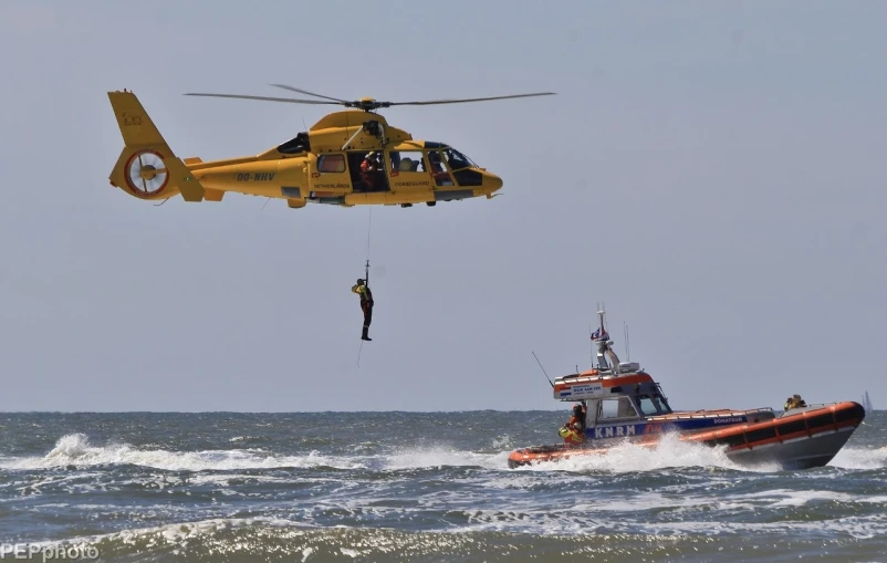 a small boat with a man attached to it near a helicopter flying above it