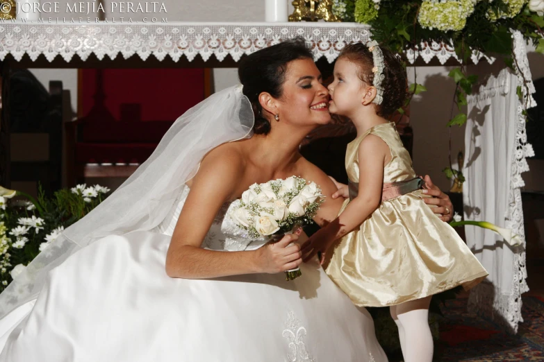 a bride in a white gown holds her daughter on the cheek