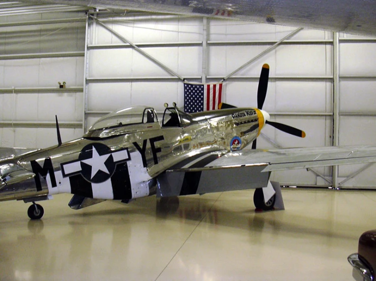 a small silver propeller airplane parked in an air hanger