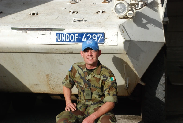 a man in camouflage sitting near a tank with a license plate