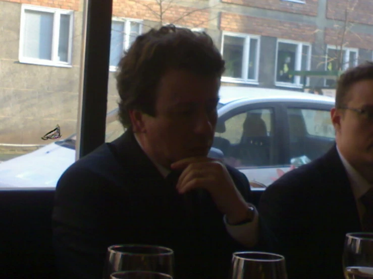 two men sitting at table in a restaurant in front of a car