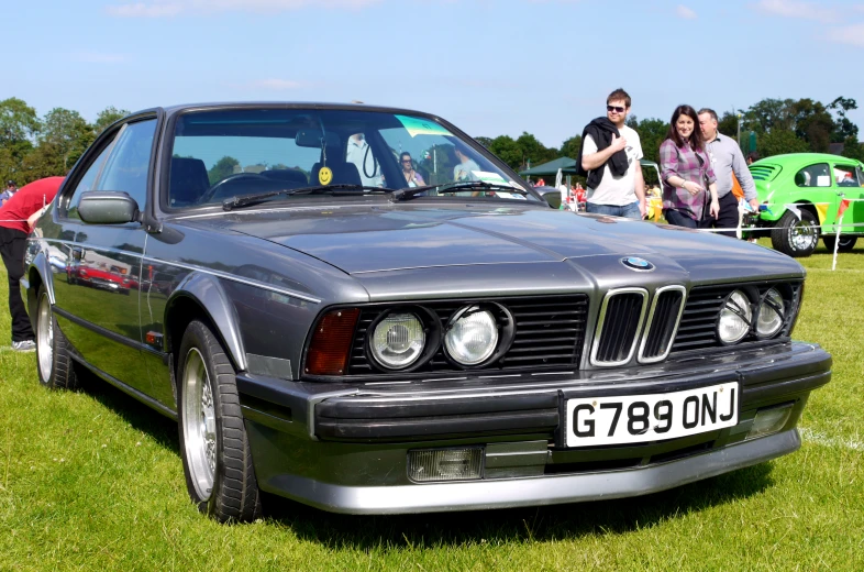 the man stands by an automobile with people looking on