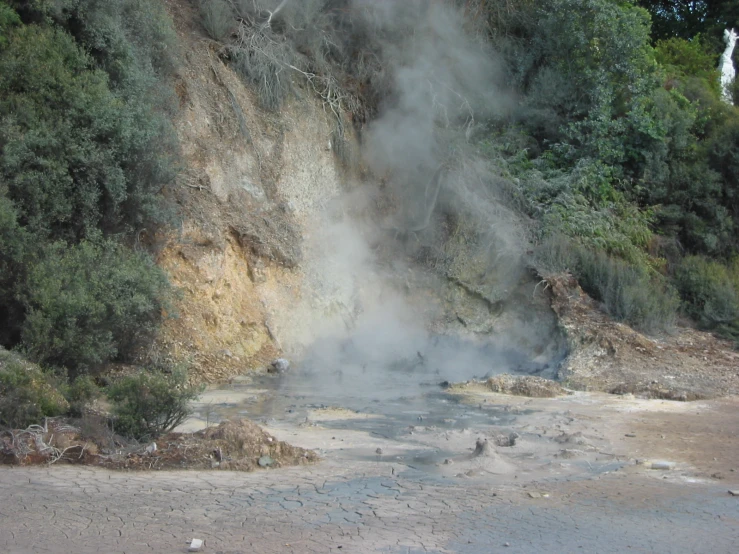 steaming water rises off the ground to the side of a cliff