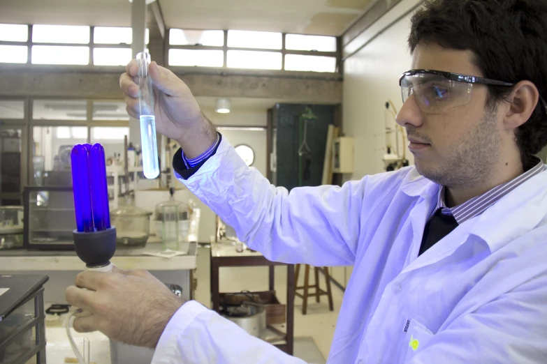 a young man in a lab coat with goggles and goggles, holding a glass tube