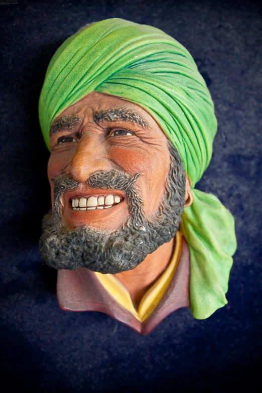an orange and green painted head with a turban and yellow scarf on
