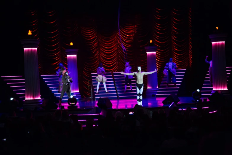 three performers on a stage that has red, white and purple lights