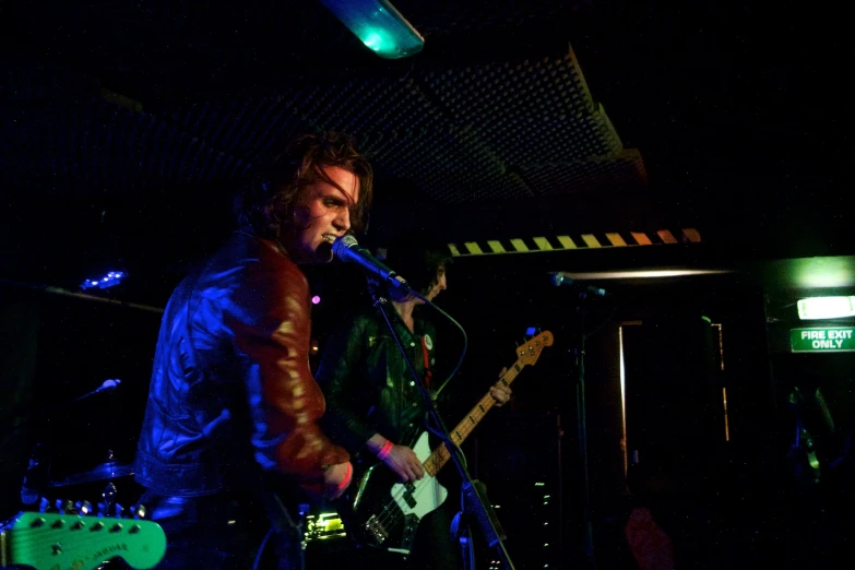 man in leather jacket singing into microphone and guitar