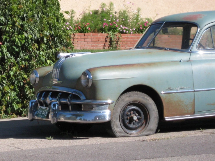 an old - fashioned car sitting on the curb with overgrown vegetation