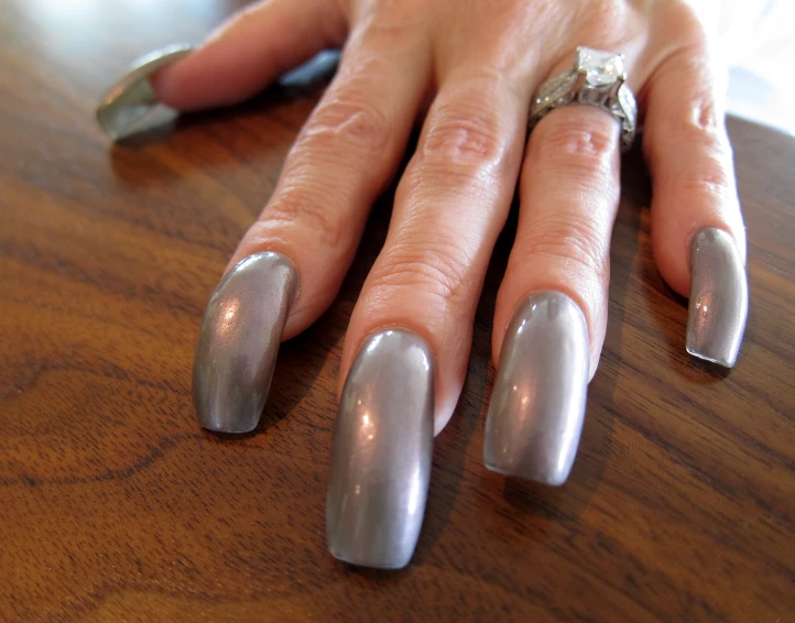 a womans silver nail polish sitting on top of a wooden table