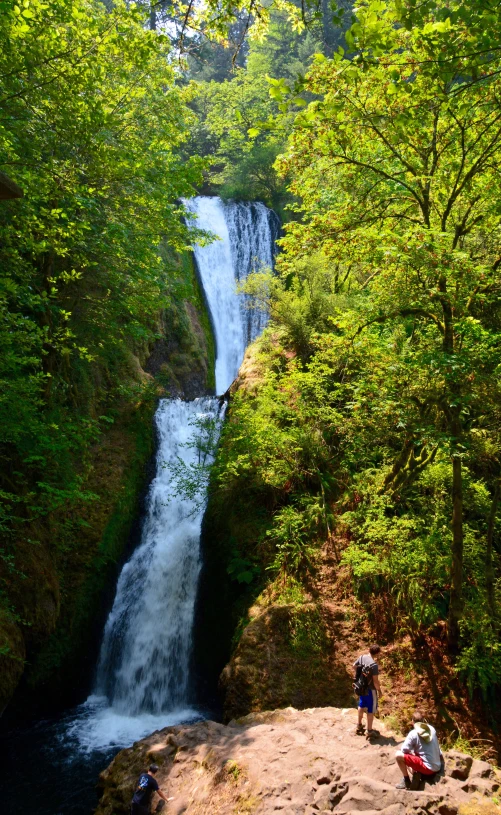 a person stands at the top of a rock beside a small waterfall