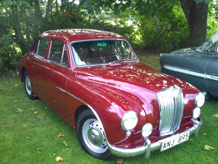 an old red car in a grassy area next to a black car