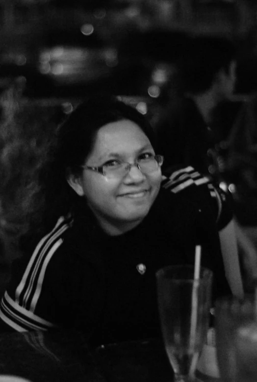 a smiling woman sitting at a table with drinks in front of her