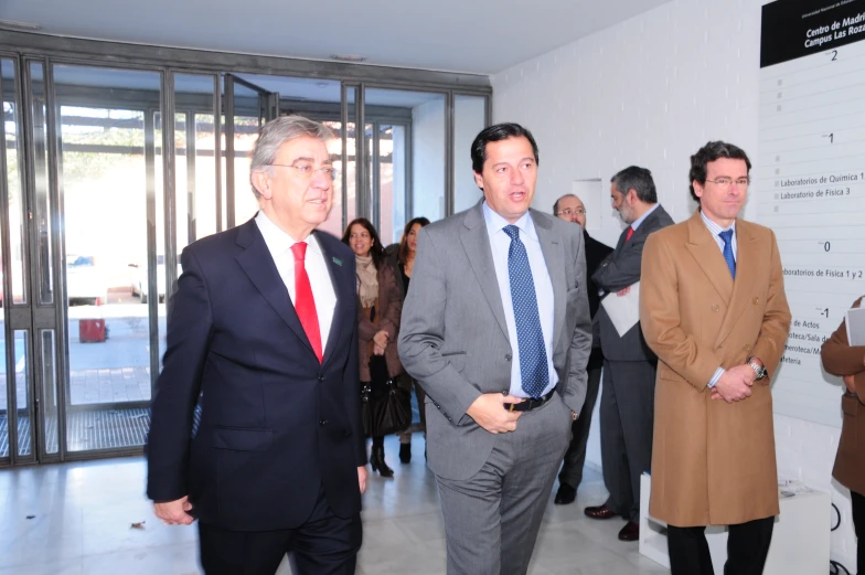 three men in business attire looking around in the middle of a group