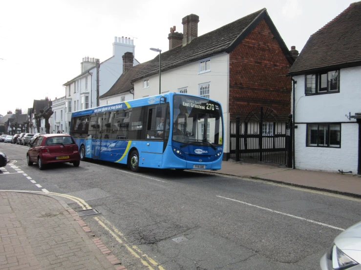 a blue bus travelling down a street next to small buildings