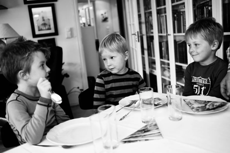 three children are eating their dinner at a table