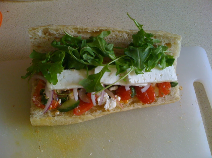 a sandwich of vegetables and cheese sits on a  board