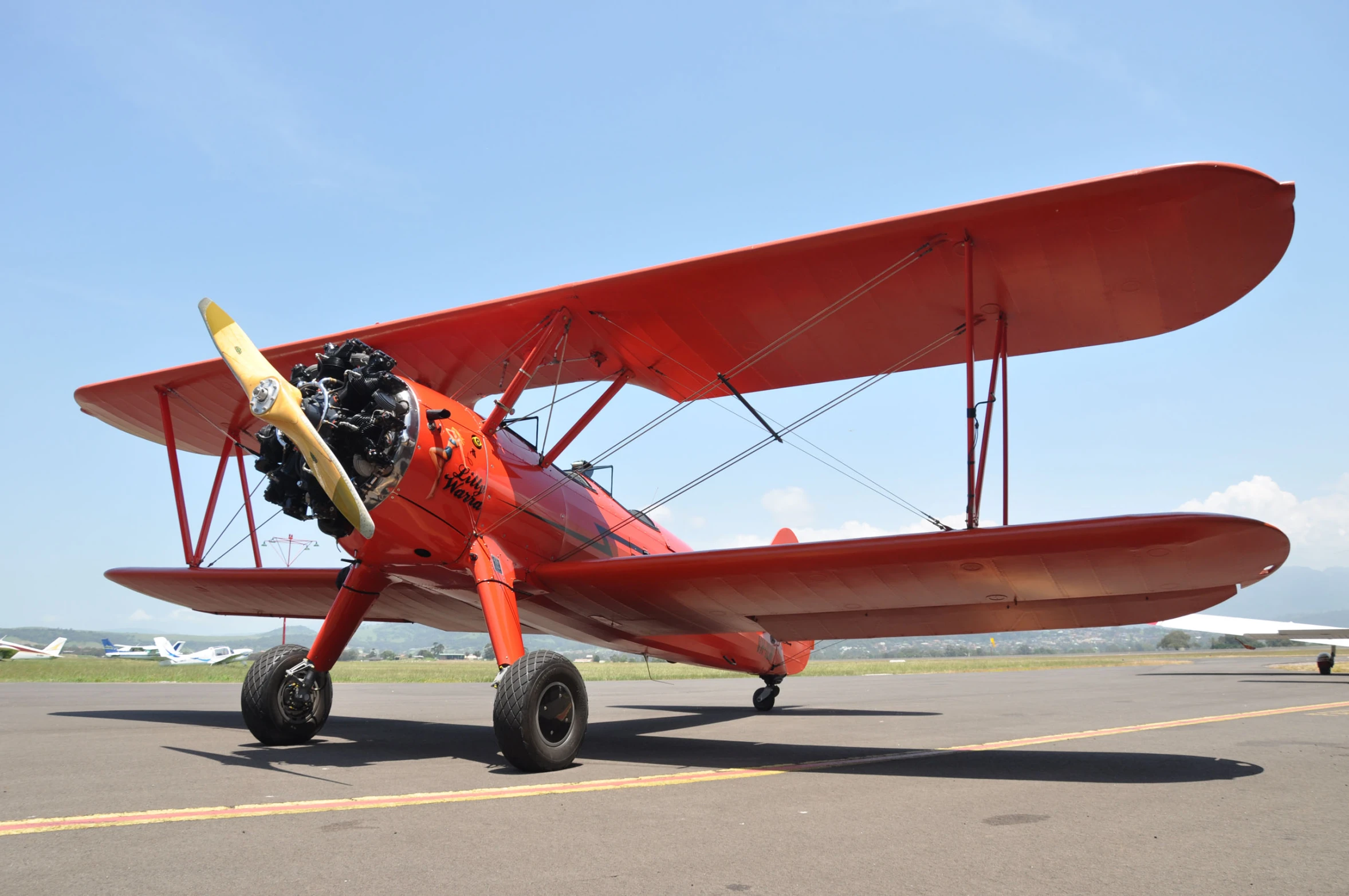 a red plane sits on a runway in the sun