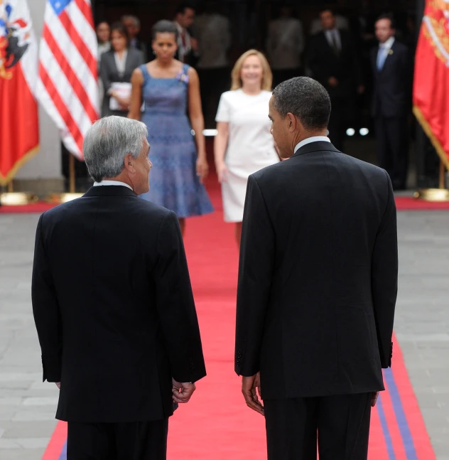 two men in suits stand on the red carpet while a woman is holding hands with a man in suit