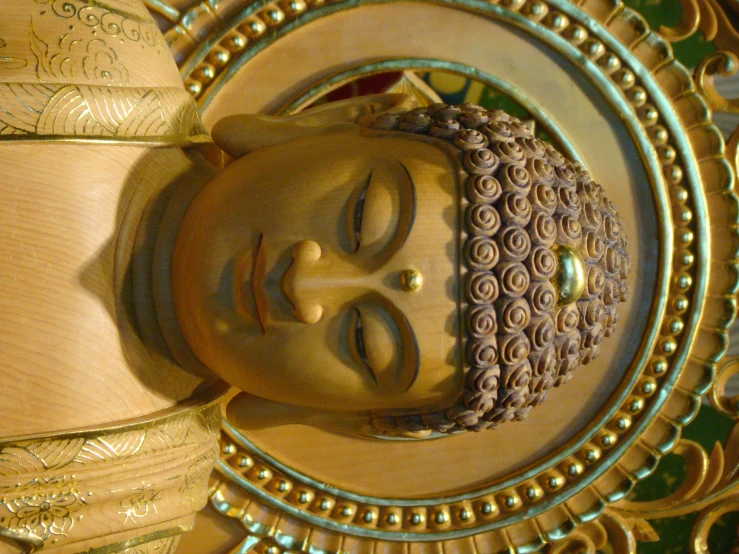 a statue of a buddhist person with a face and arms, under golden decorations