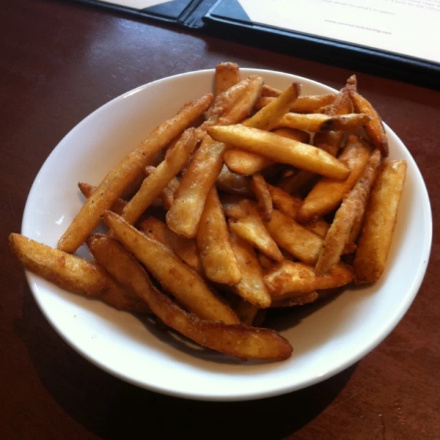 some cooked fries in a white bowl on a wooden table