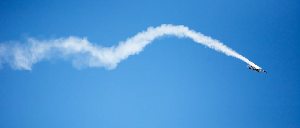 an airplane leaving a trail of smoke in the blue sky