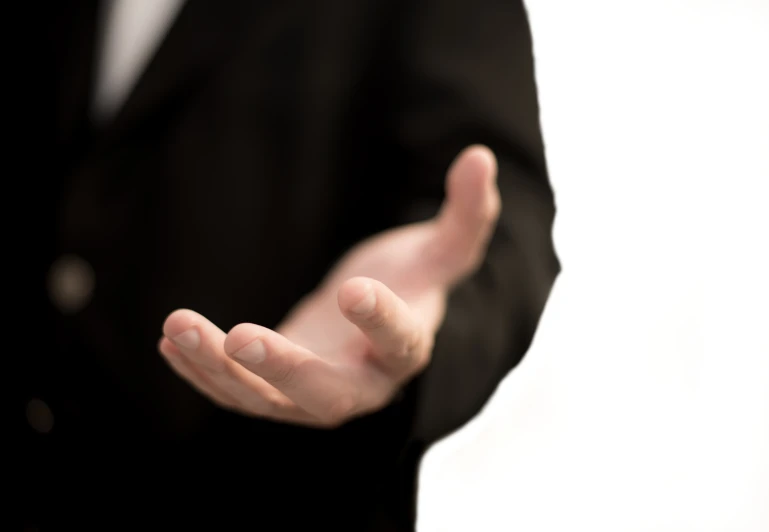 a man in black suit making an open hand gesture