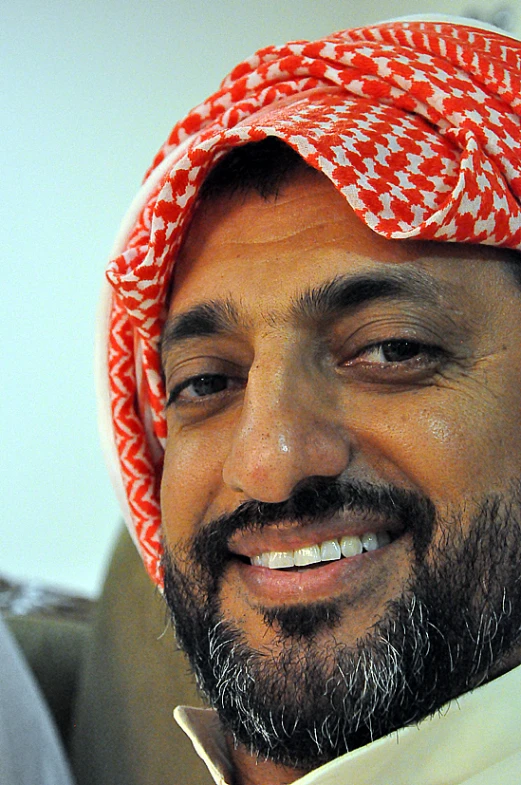 a man wearing an orange and white turban smiles into the camera