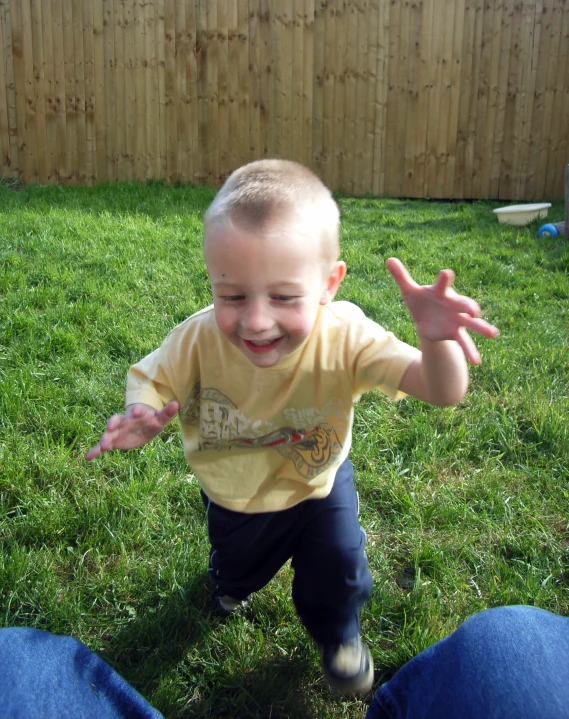 a toddler standing in the grass with his hands out