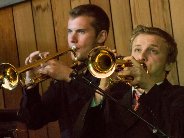 a man plays a trumpet with another man watching him