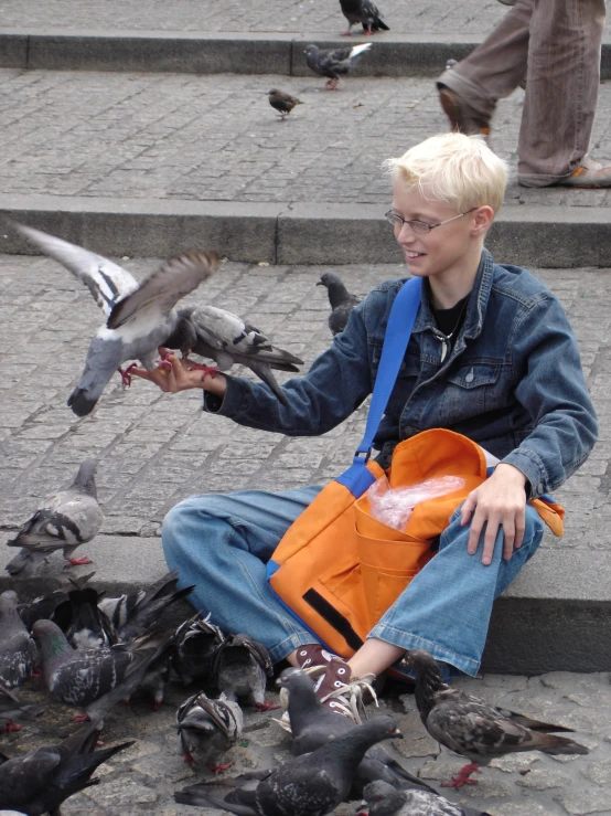 a boy sitting in front of pigeons and birds