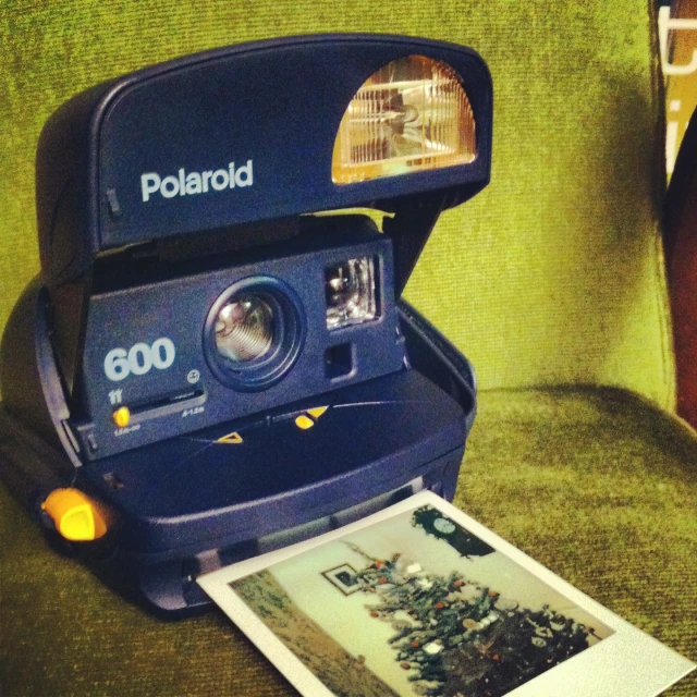 a polaroid camera sitting on top of a green chair next to a polaroid print