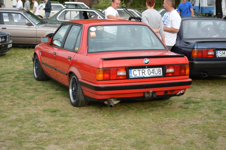 an orange bmw with two passengers standing behind it