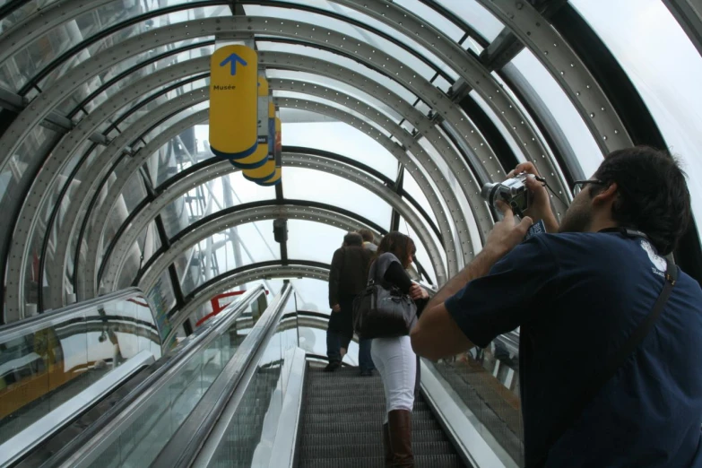 people on escalator with camera equipment on the bottom