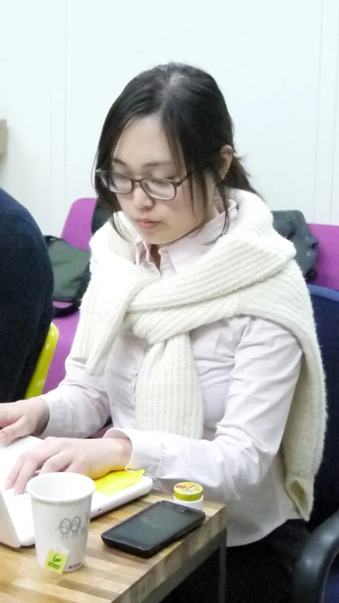 the woman is sitting at a table with a book, laptop and cup on it