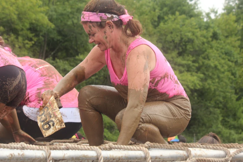 three women in muddy outfits hold onto a wall