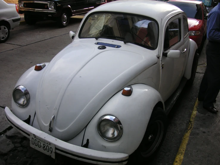 a white beetle car sitting next to a man in a blue shirt